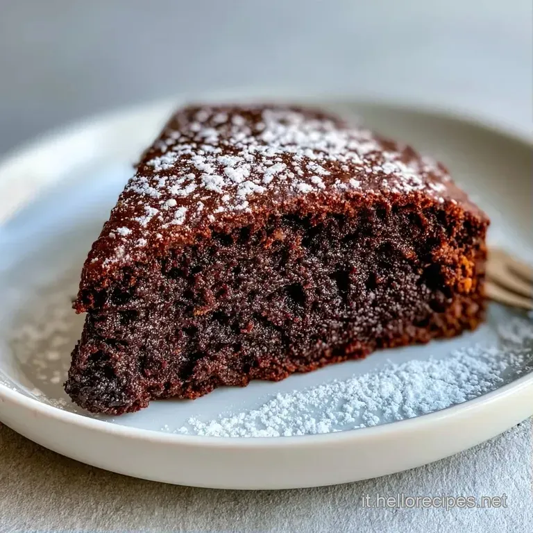 Fetta di torta al cioccolato dalla consistenza densa su piatto bianco, decorata con un lampone rosso e foglia di menta.